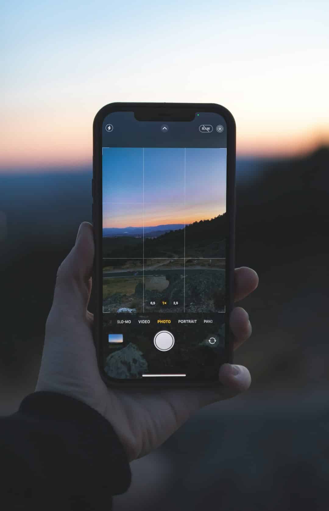 Handheld smartphone displaying a photo app with a grid over a sunset landscape.