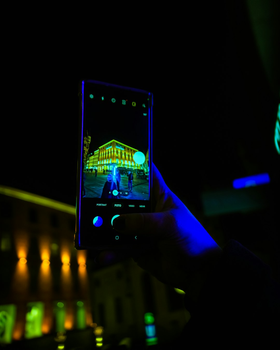 Person holds a smartphone at night, capturing a neon-lit building reflected on the screen's display.