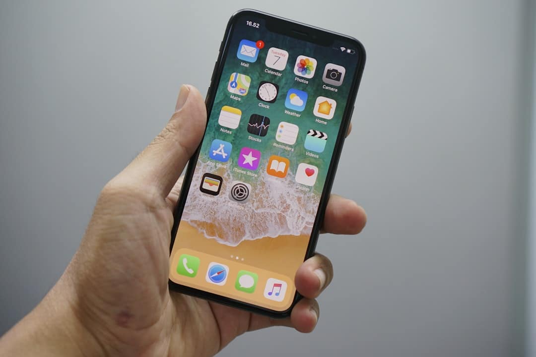 Hand holding a smartphone showing the home screen with app icons on a sandy wallpaper background.