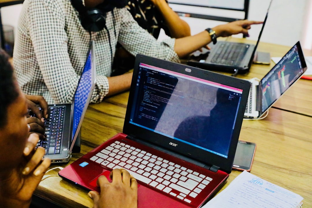 Group of people coding on laptops at a wooden table in a collaborative workspace.