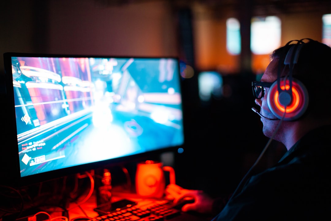Gamer wearing a headset with glowing red ear cups, intensely focused on a neon-lit computer game on a large monitor.
