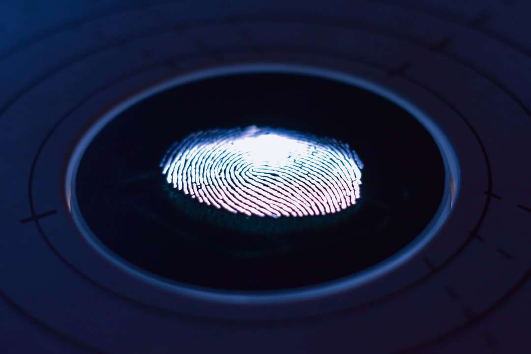 Close-up of a fingerprint on a biometric scanner, illuminated in blue light.