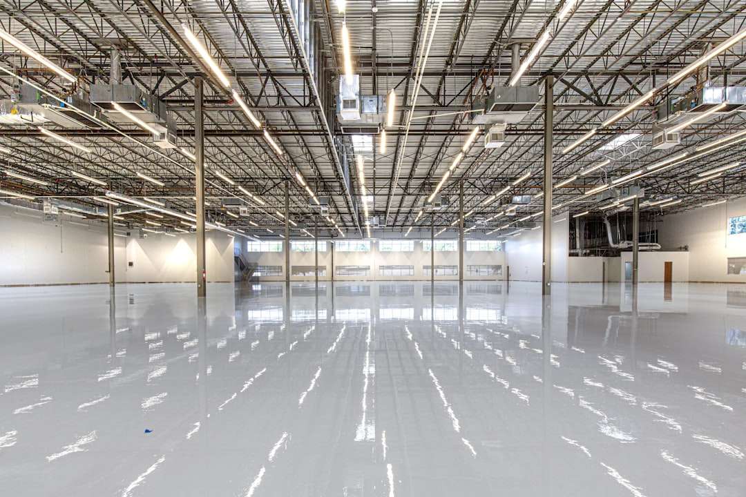 Empty industrial warehouse interior with a glossy white floor, steel columns, and bright overhead lights.