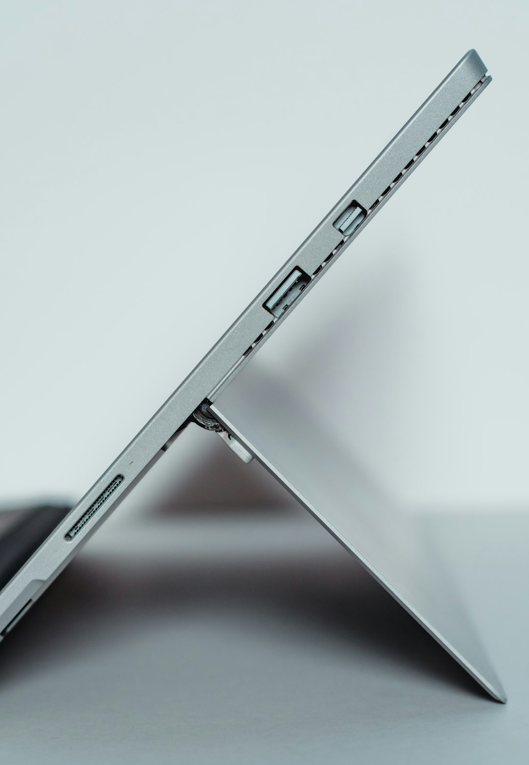 Slim silver 2-in-1 laptop/tablet propped on its kickstand, shown from the side with visible edge ports