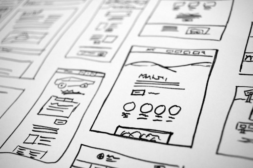 Black-and-white sketch of multiple web page wireframes laid out on a table, showing UI blocks and icons.