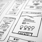Black-and-white sketch of multiple web page wireframes laid out on a table, showing UI blocks and icons.