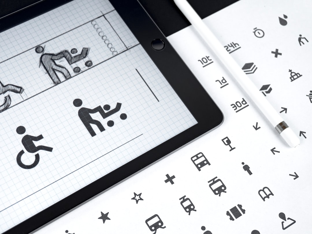 Tablet showing wireframe sketches of accessibility icons on a grid, with a pencil nearby on a design surface.