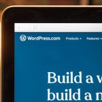 Laptop screen showing WordPress.com homepage with blue navigation bar and a large white 'Build a website' headline on a blue background.