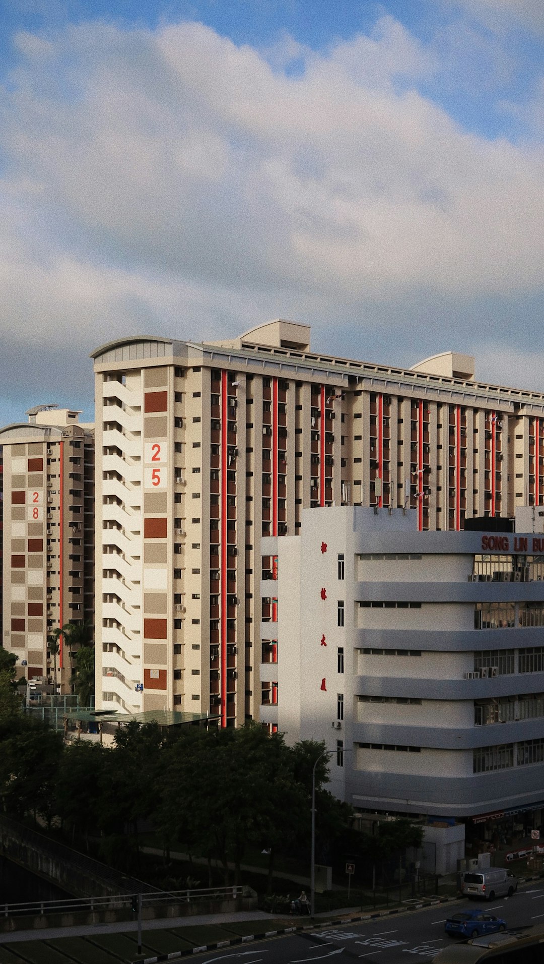 Tall beige apartment complex with red vertical accents against a blue sky. consist of multiple high-rise towers with balconies and stairwells.