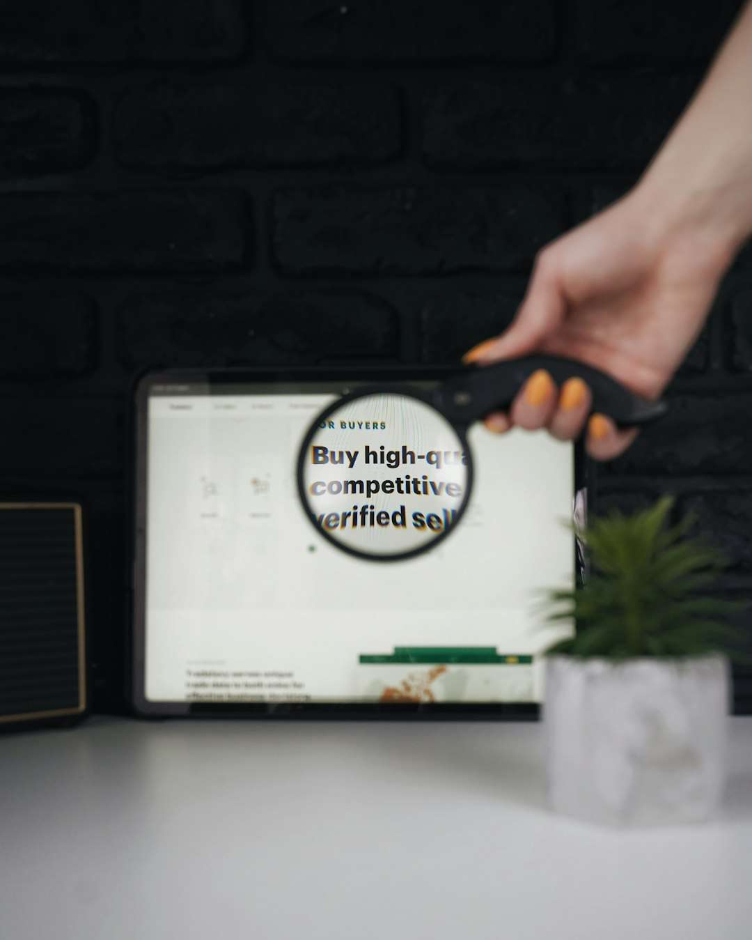 Person uses a magnifying glass to zoom in on a tablet screen displaying a 'Buy high-quality competitive' message about trusted sellers.