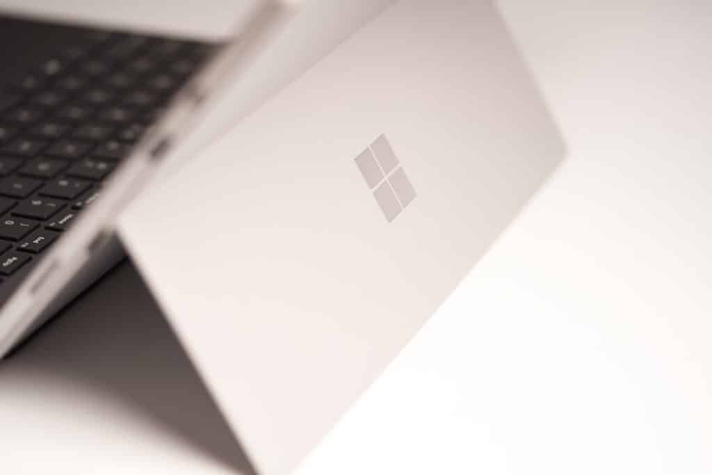 Close-up of a silver laptop lid featuring a subtle Windows logo, photographed at an angle.