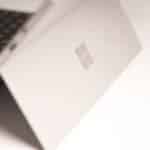 Close-up of a silver laptop lid featuring a subtle Windows logo, photographed at an angle.