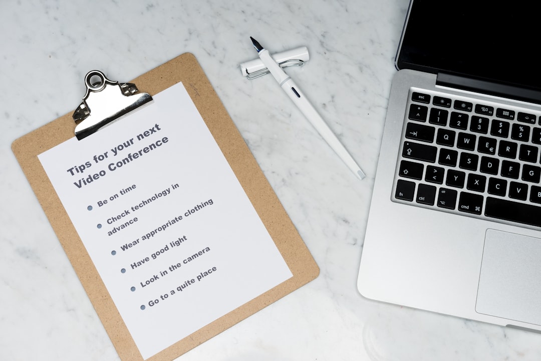Clipboard with a printed list titled 'Tips for your next Video Conference' beside a white pen and a laptop on a marble desk, suggesting meeting prep tips.
