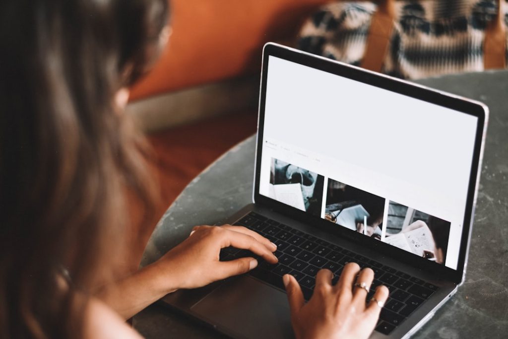Person typing on a laptop at a table, viewing a photo gallery on the screen.