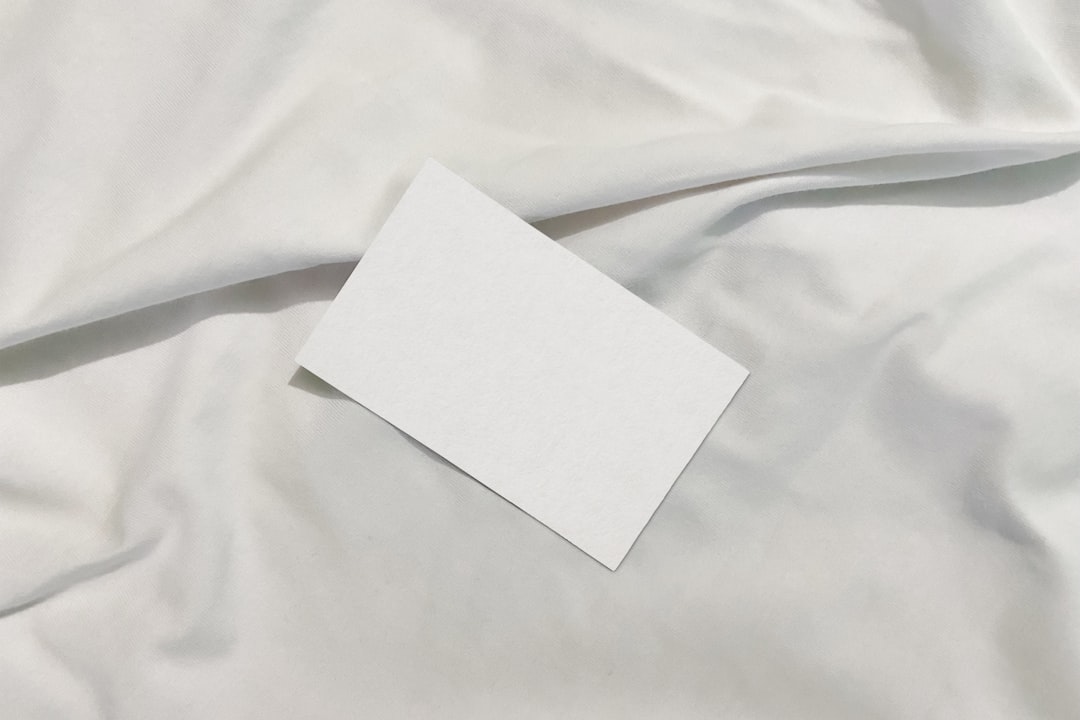 Blank white business card placed diagonally on a soft white fabric surface, empty and ready for text.