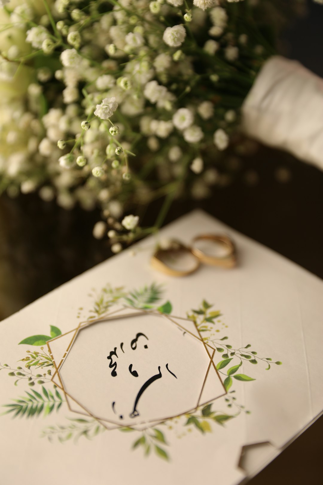 Wedding invitation with botanical wreath and wedding rings resting nearby on a table.