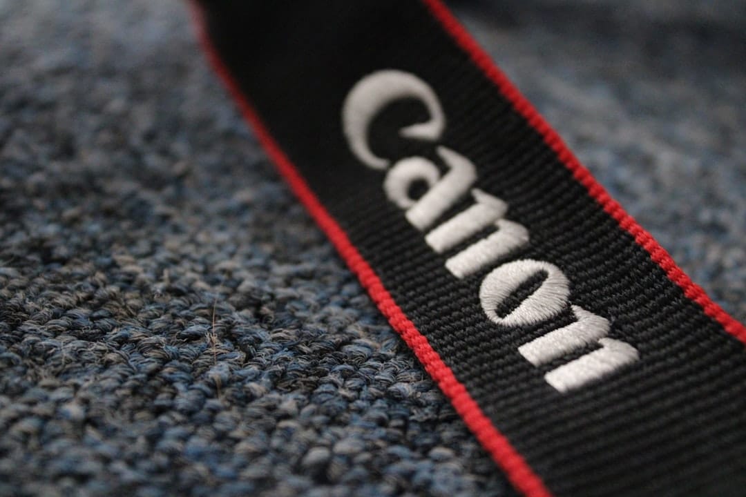 Close-up of a black Canon camera strap with white lettering and a red edge on a blue textured surface.