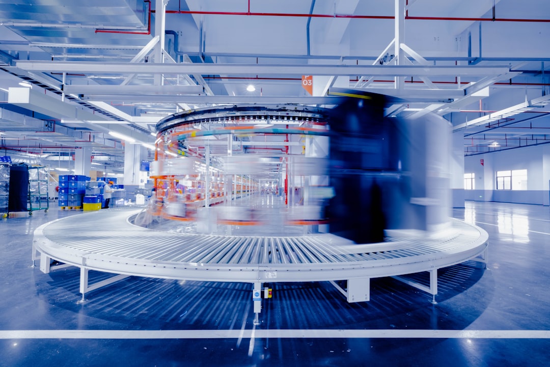 Circular automated conveyor loop at the center of a bright industrial facility, with blurred motion suggesting moving goods and workers in the background.