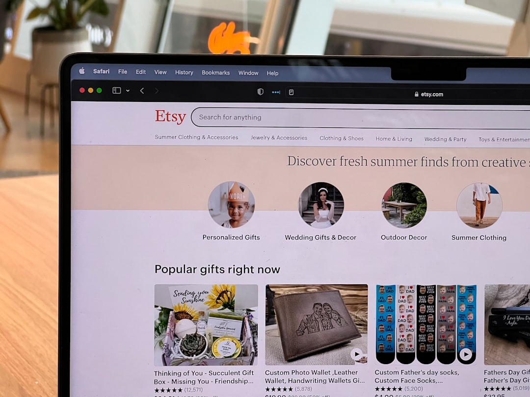 Laptop screen showing Etsy homepage with category icons and search bar on a wooden desk