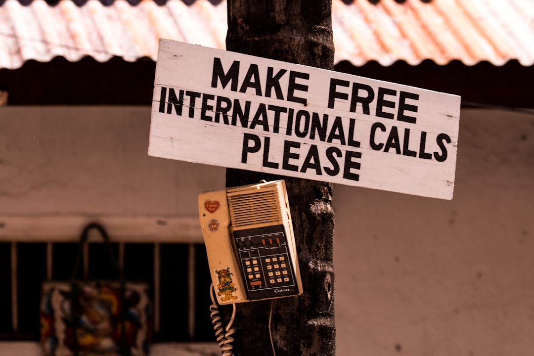 Sign on a pole asking for free international calls, with an old payphone attached nearby in a sunny outdoor setting.