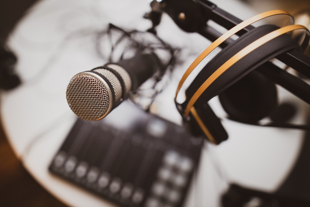 Close-up of a microphone on a stand with gold headphones resting on it in a recording studio setting.
