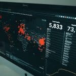 Dark dashboard on a monitor showing a world map with red outbreak markers and right-side stats for deaths and recoveries (e.g., 5,833 deaths; 73,968 recovered).
