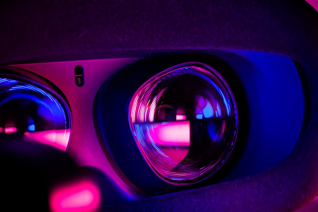 Close-up of a virtual reality headset lens illuminated by pink and blue neon lights.