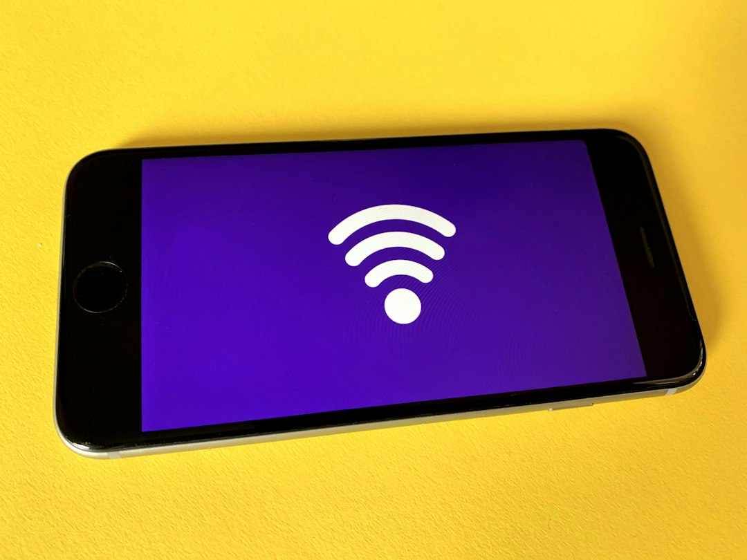 Smartphone lying on a yellow surface, screen shows a white Wi‑Fi symbol on a purple background.