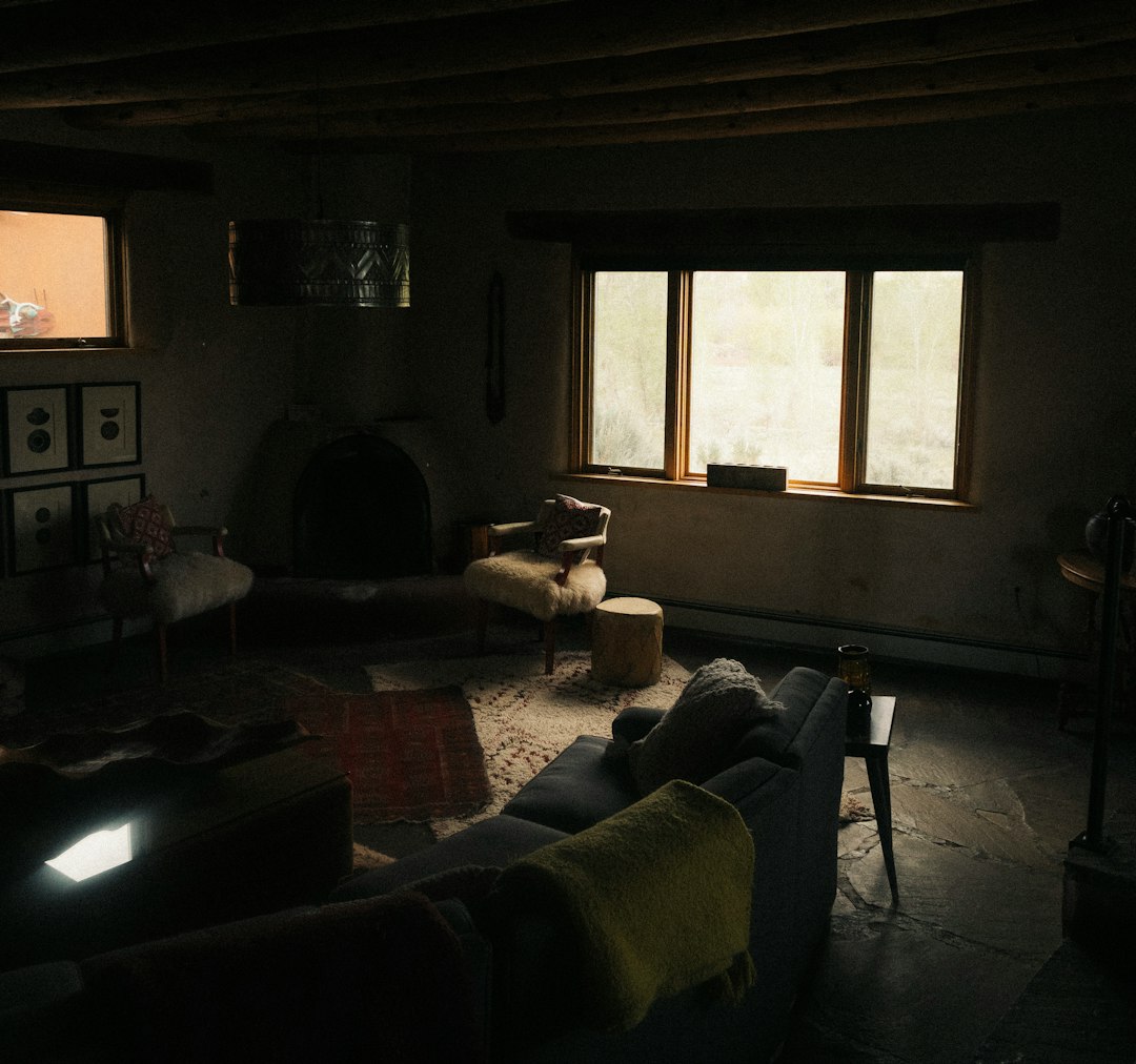Dim living room with a large window, a fireplace, and fur-covered chairs arranged around a rug.