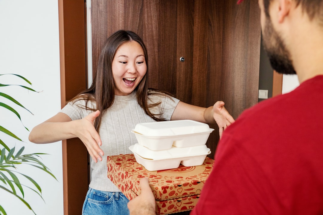 Woman at a doorway receiving a stacked pizza box and white takeout containers, smiling with excitement as the delivery arrives.