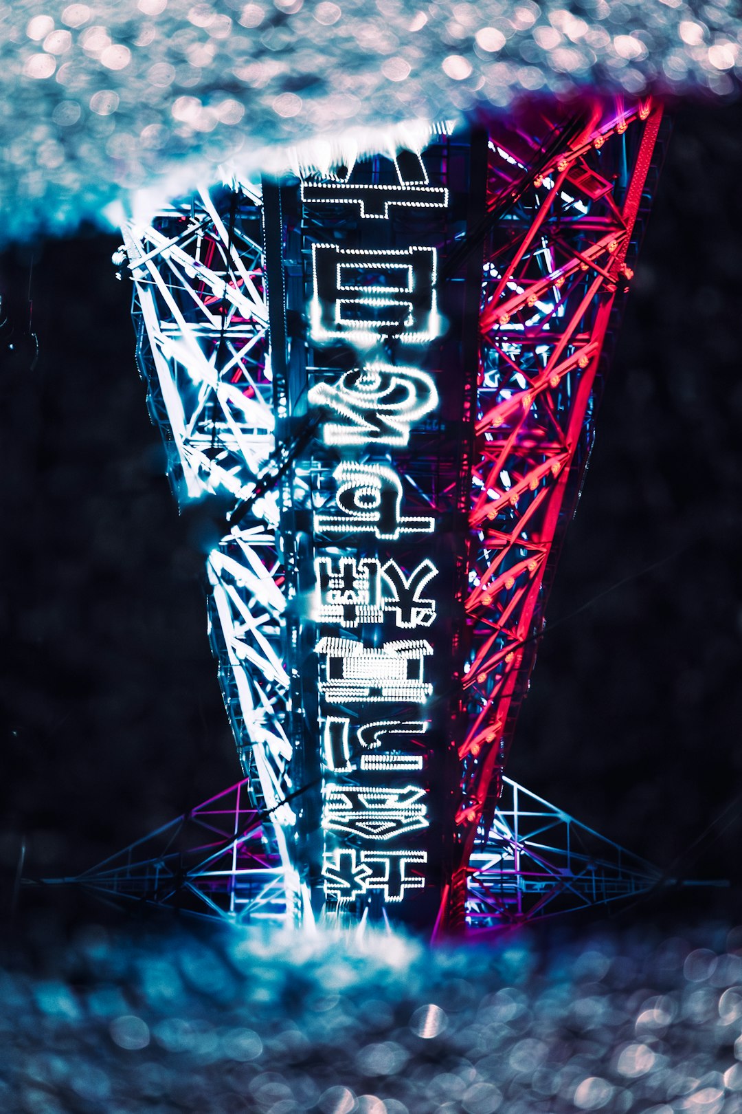 Neon-lit vertical sculpture with blue and pink lights and glowing characters at night (art installation).