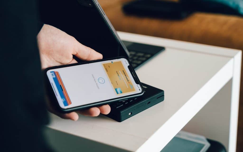 Person using a smartphone on a card reader to make a contactless payment on a white table edge.
