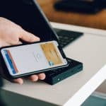 Person using a smartphone on a card reader to make a contactless payment on a white table edge.