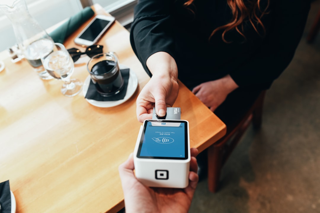 Customer paying with a contactless card on a white payment terminal at a cafe table, with a coffee mug nearby.