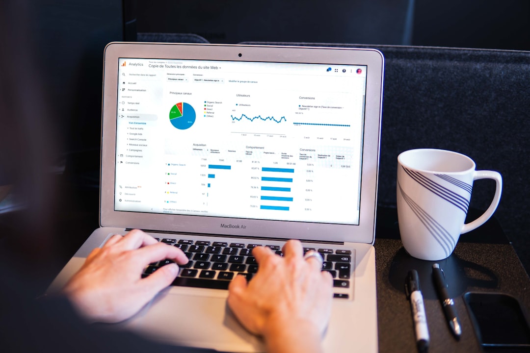 Person typing on a MacBook Air showing an analytics dashboard with charts; a striped mug sits to the right on the desk.