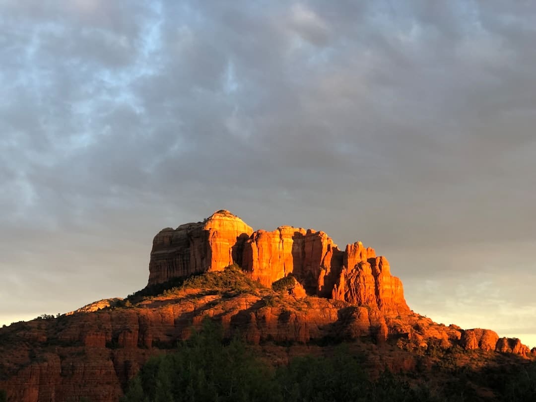 Red sandstone mesa bathed in warm sunset light against a cloudy sky.