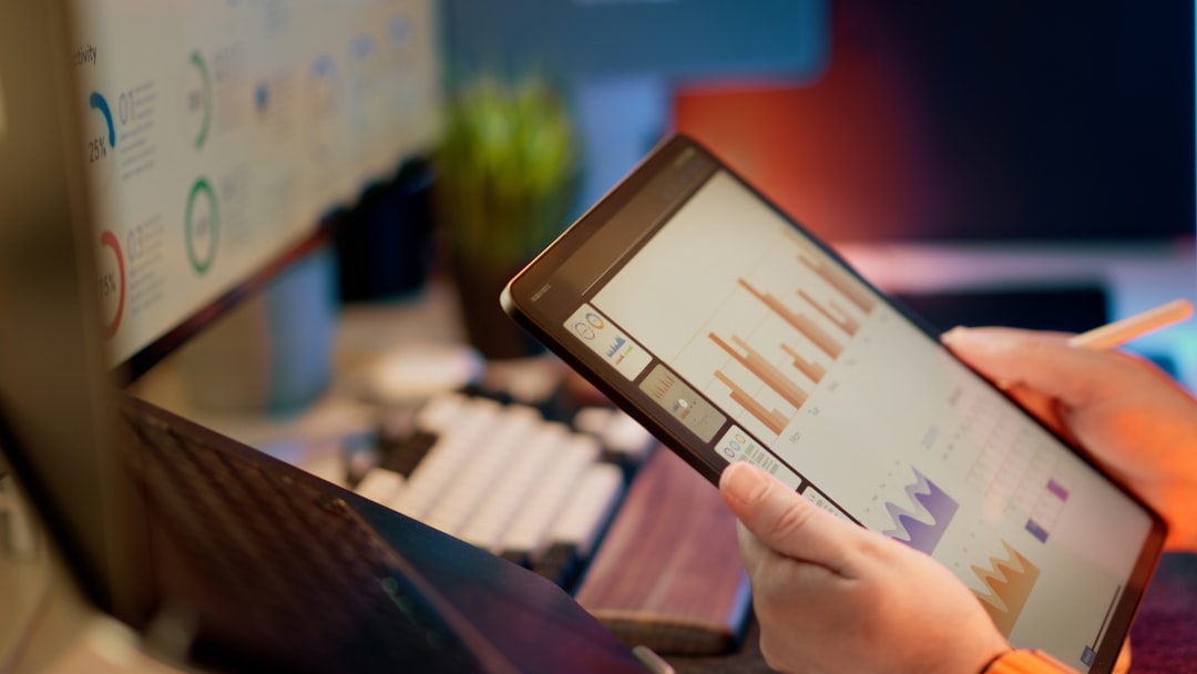 Person holds a tablet displaying bar charts and graphs in an office dashboard setting.