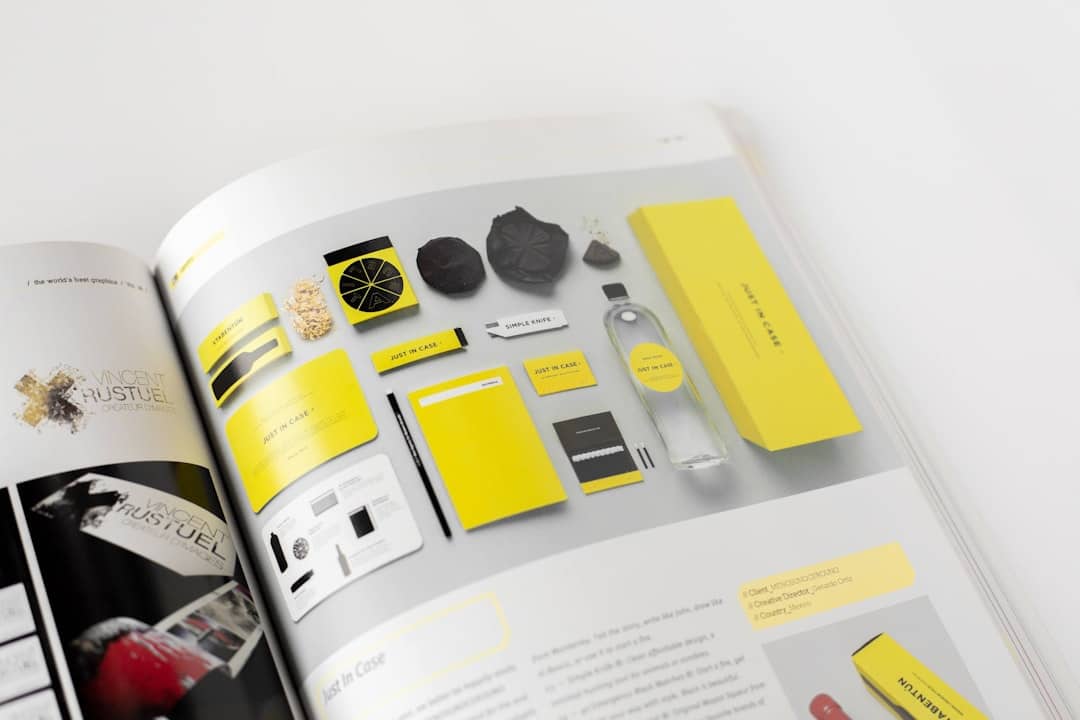 Branding mockup with yellow packaging, notebooks, and a bottle laid out on a gray spread in a magazine.”] ,
