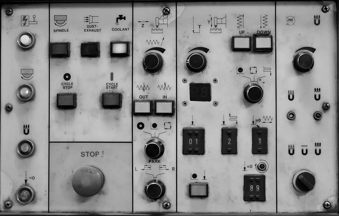 Industrial control panel with multiple switches and knobs labeled for spindle, dust exhaust, and coolant, plus cycle start/stop buttons and a large STOP button below a gray reset dial.
