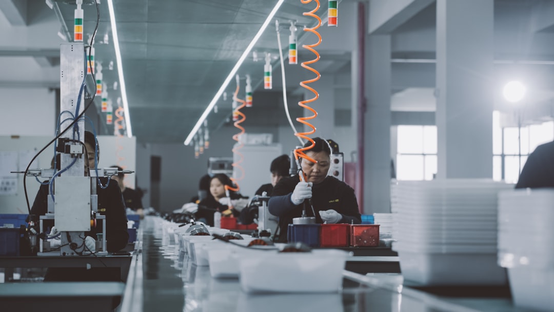 Factory assembly line with workers at stations assembling products under bright overhead lights.