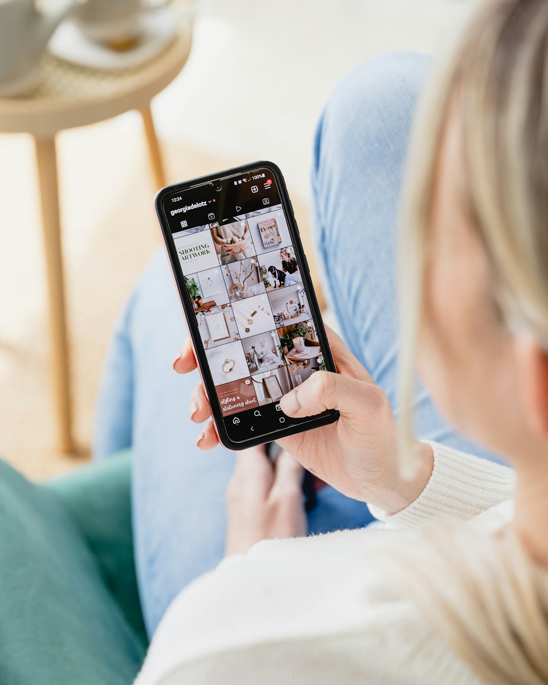 Person holds a smartphone displaying a grid-style Instagram feed of photos.