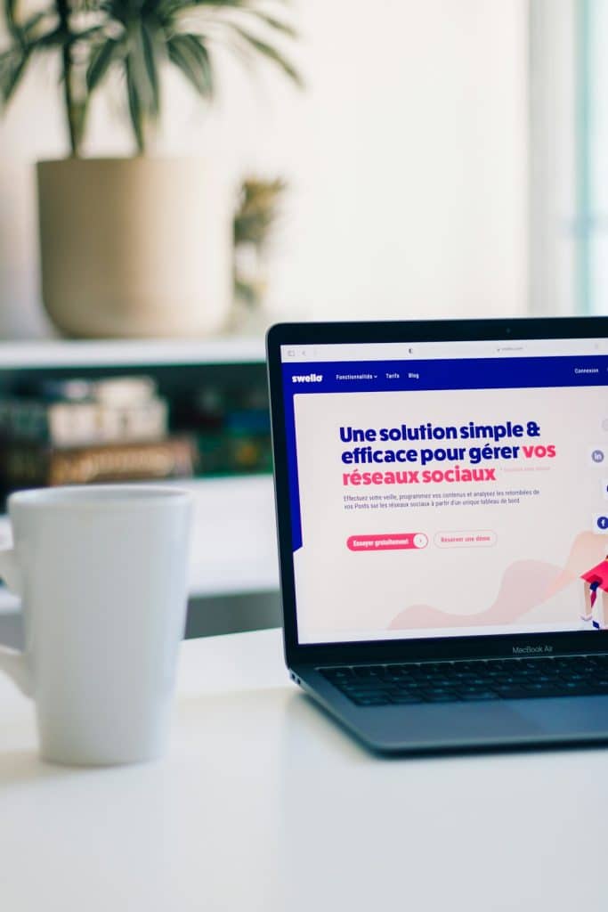 Laptop on a white desk showing a French marketing webpage about social networks in bold blue and pink text.