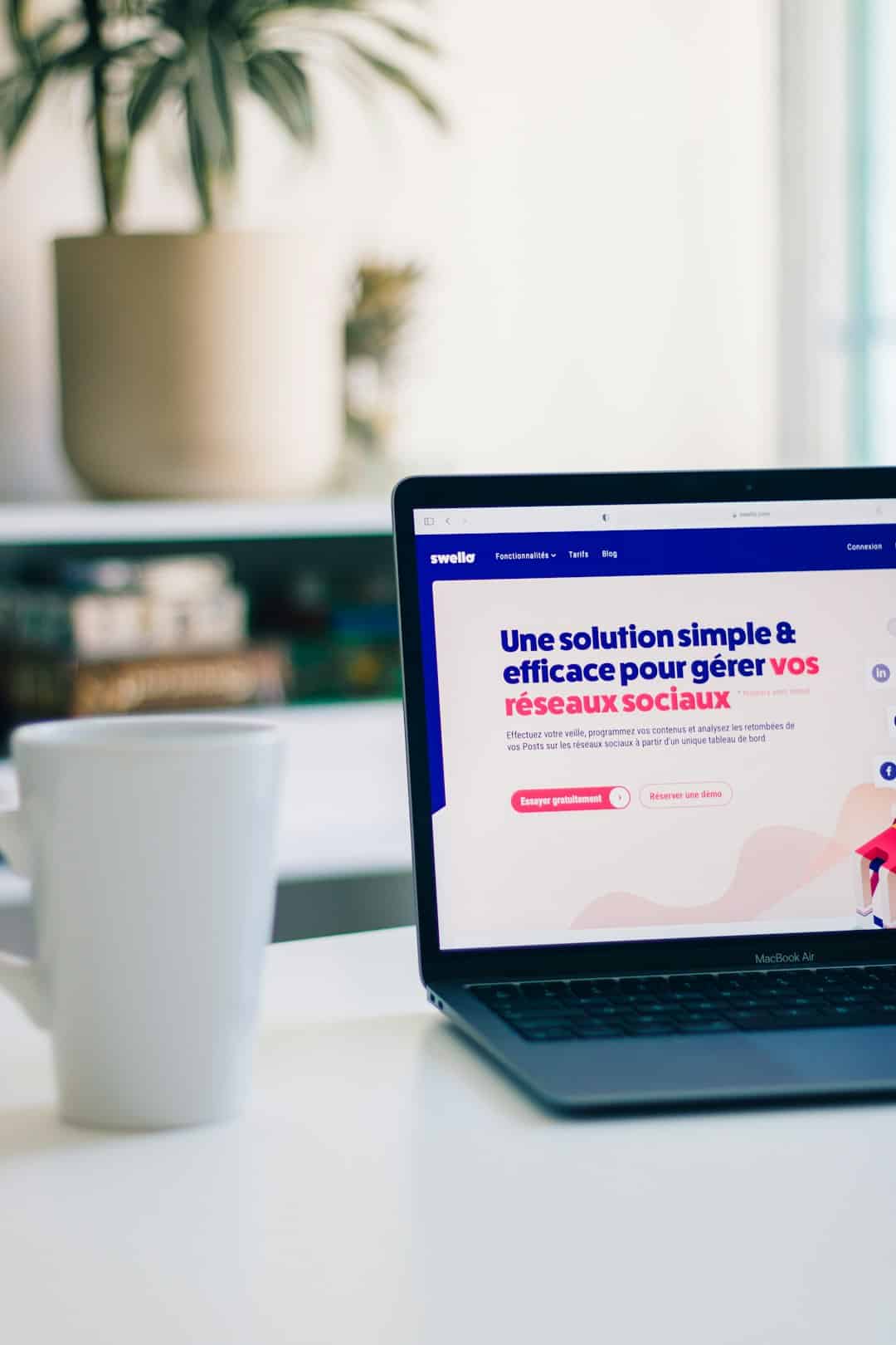 Laptop on a white desk showing a French marketing webpage about social networks in bold blue and pink text.