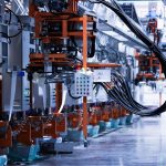 Industrial robotics line with orange-framed machinery and hanging cables in a factory.