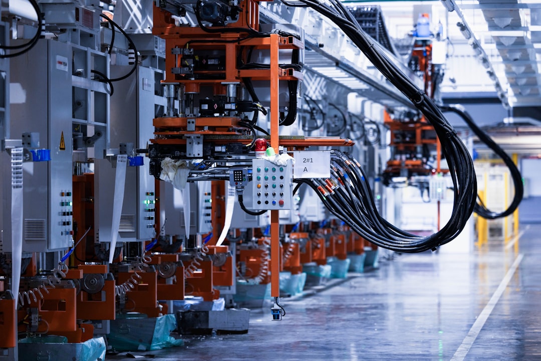 Industrial robotics line with orange-framed machinery and hanging cables in a factory.