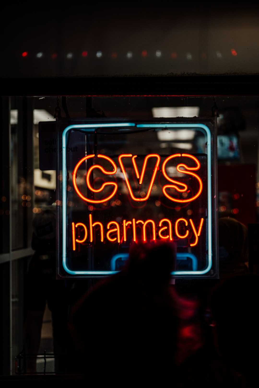 Red neon CVS Pharmacy sign in a storefront window at night, with a blue border.