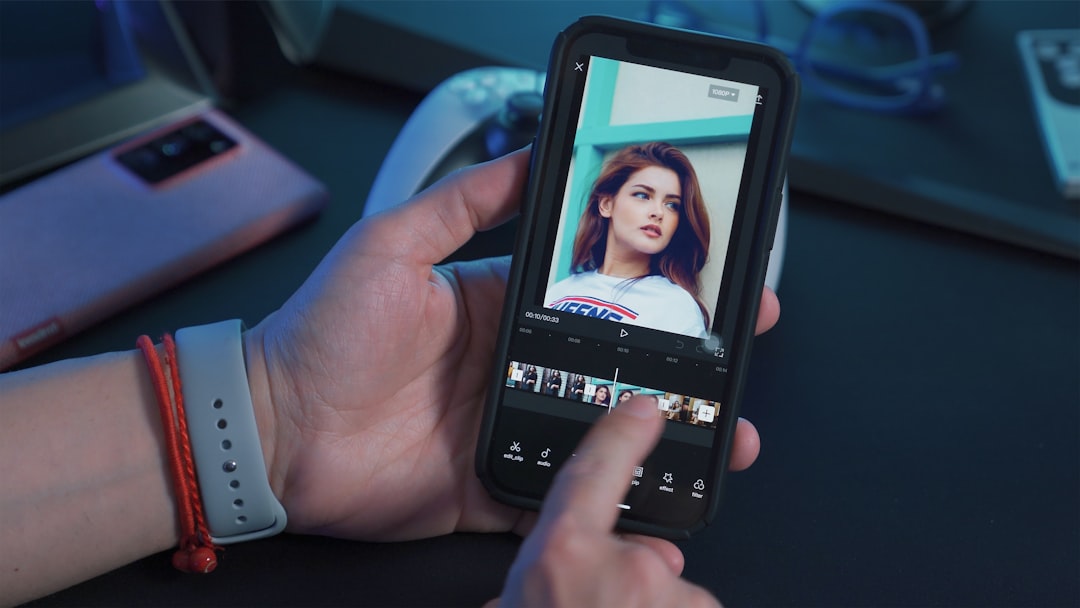 Hand holding a smartphone with a video editing app open, showing a portrait on screen and a timeline below.