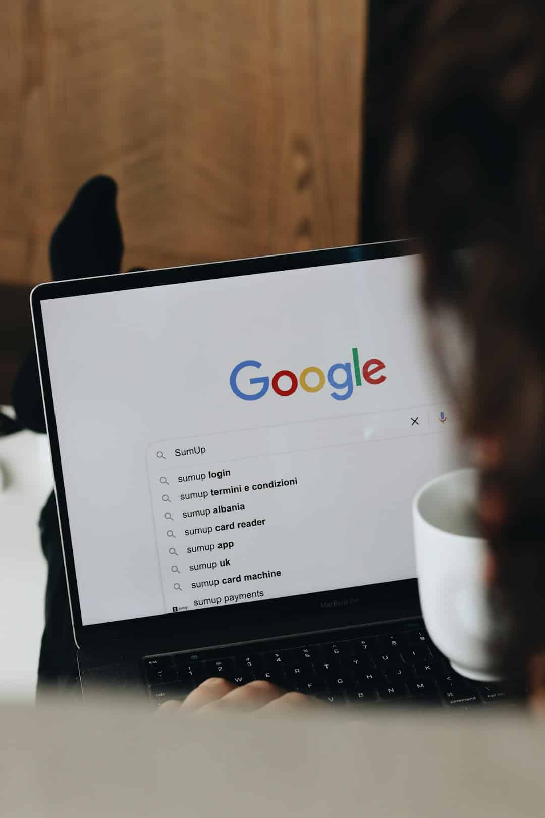 Person using a laptop displaying the Google homepage with a search suggestions list on screen.