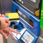 Person inserting a card into an ATM machine for a cash withdrawal or transaction.