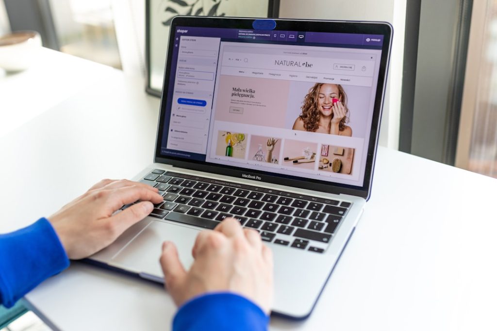Person uses a MacBook Pro to browse an online beauty store homepage with a large banner image.